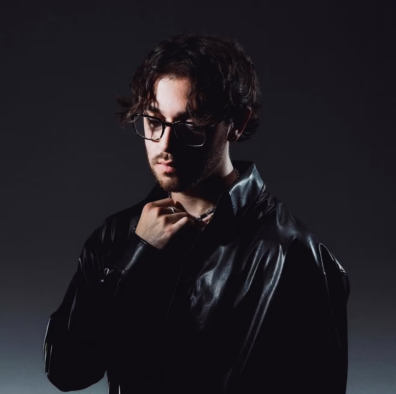 Chris-Grey-artist-bio-profile-wearing-glasses-and-black-suit-eery-grey-background