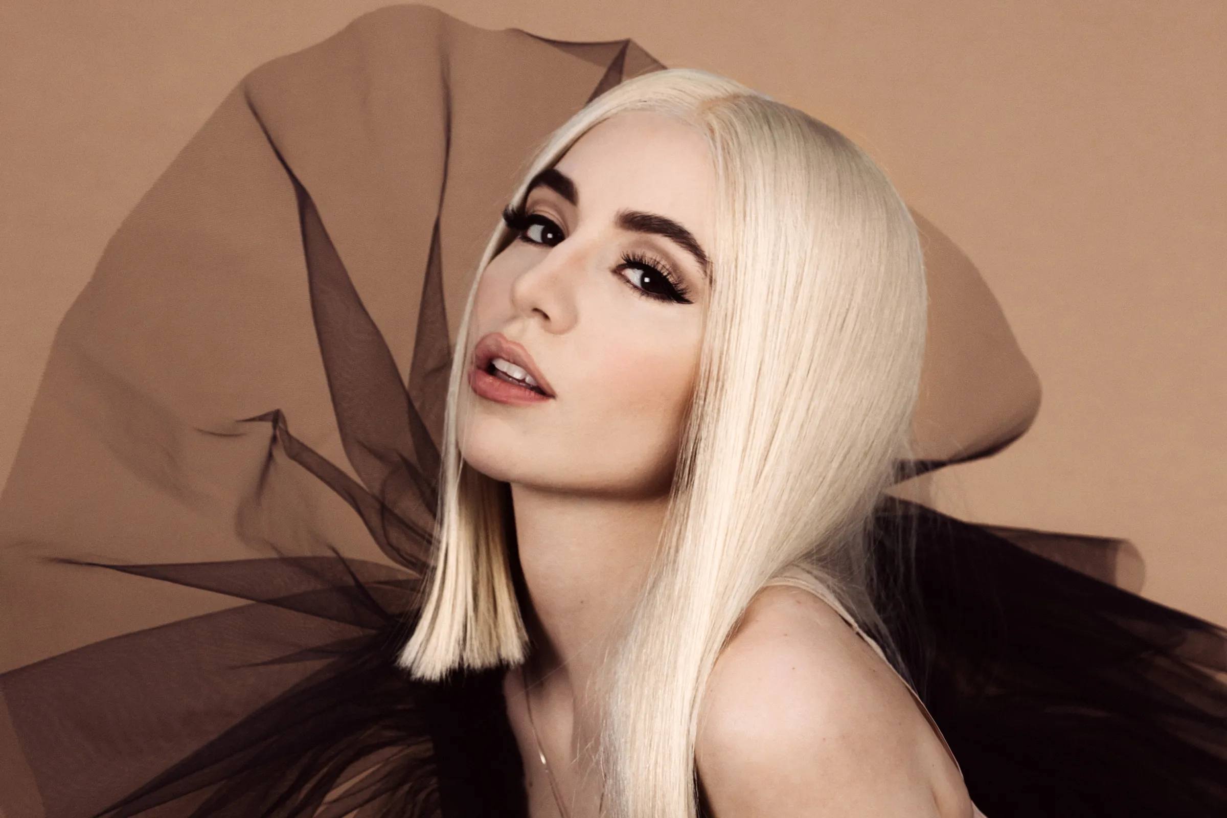 Ava Max in puffy black dress, nude make up, signature blond asymmetric "Ava Cut", neutral background