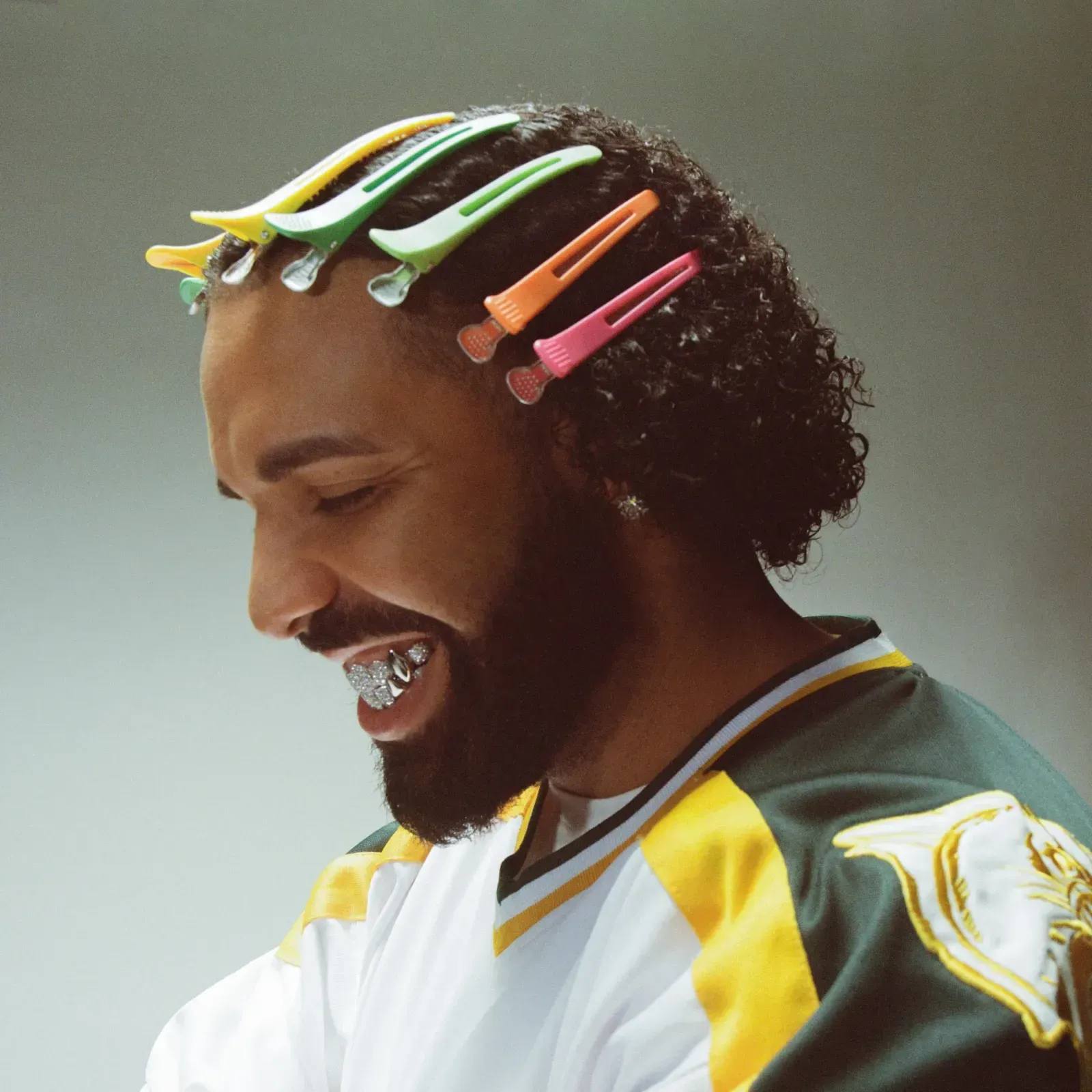 Drake's smiling face wearing a rainbow colored set of hairpins on his head