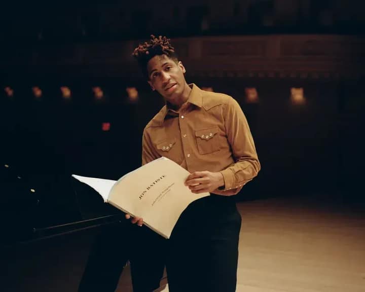Jon Batiste on stage holding notes of his composition