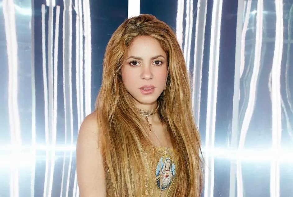 Shakira in a gold dress against silver backdrop