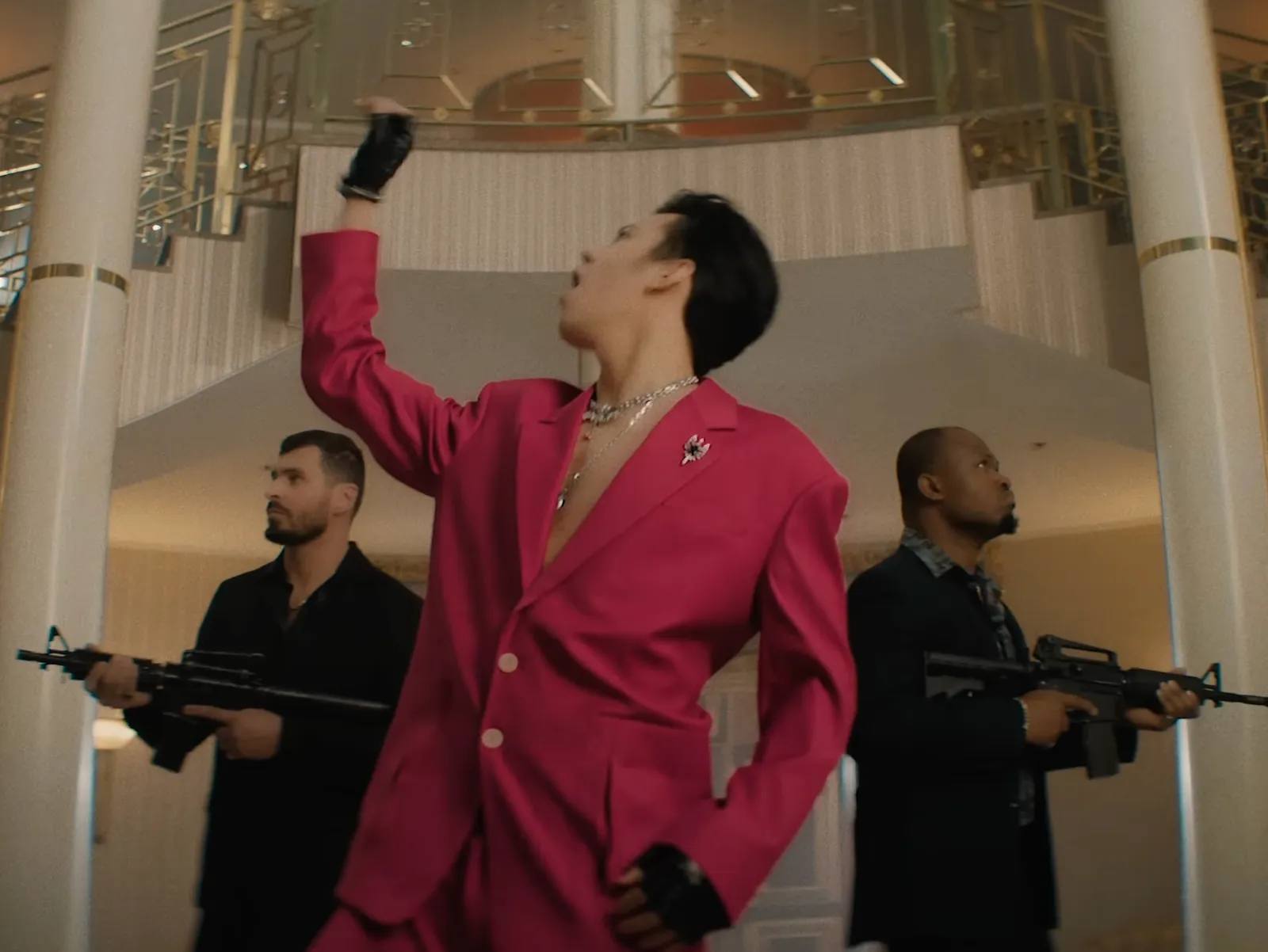 Dimash Kudaibergen wearing red oversized suit with sleek hairstyle, surrounded by armed men in music video 'Smoke', released May 29, 2024