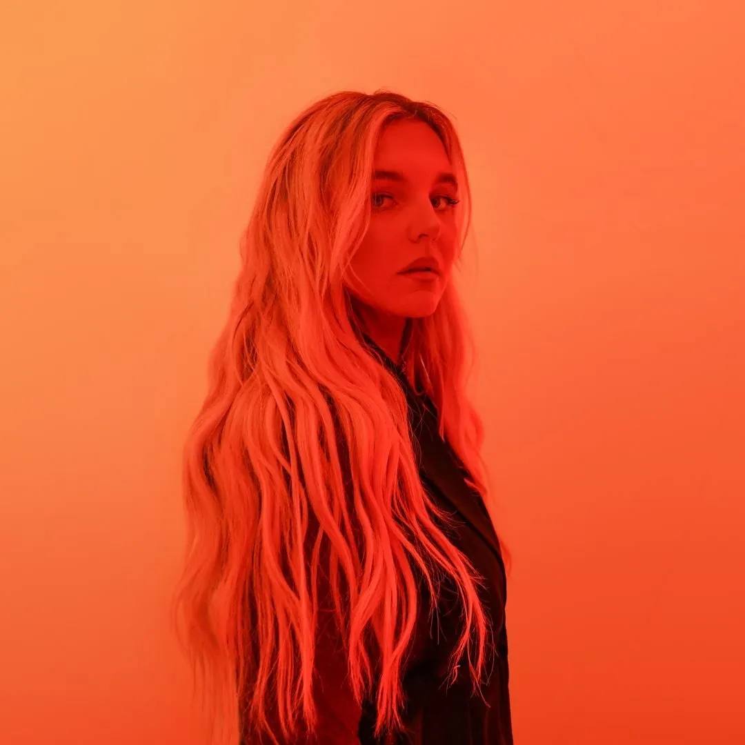 Tones and I portrait, long blond hair, bright orange background