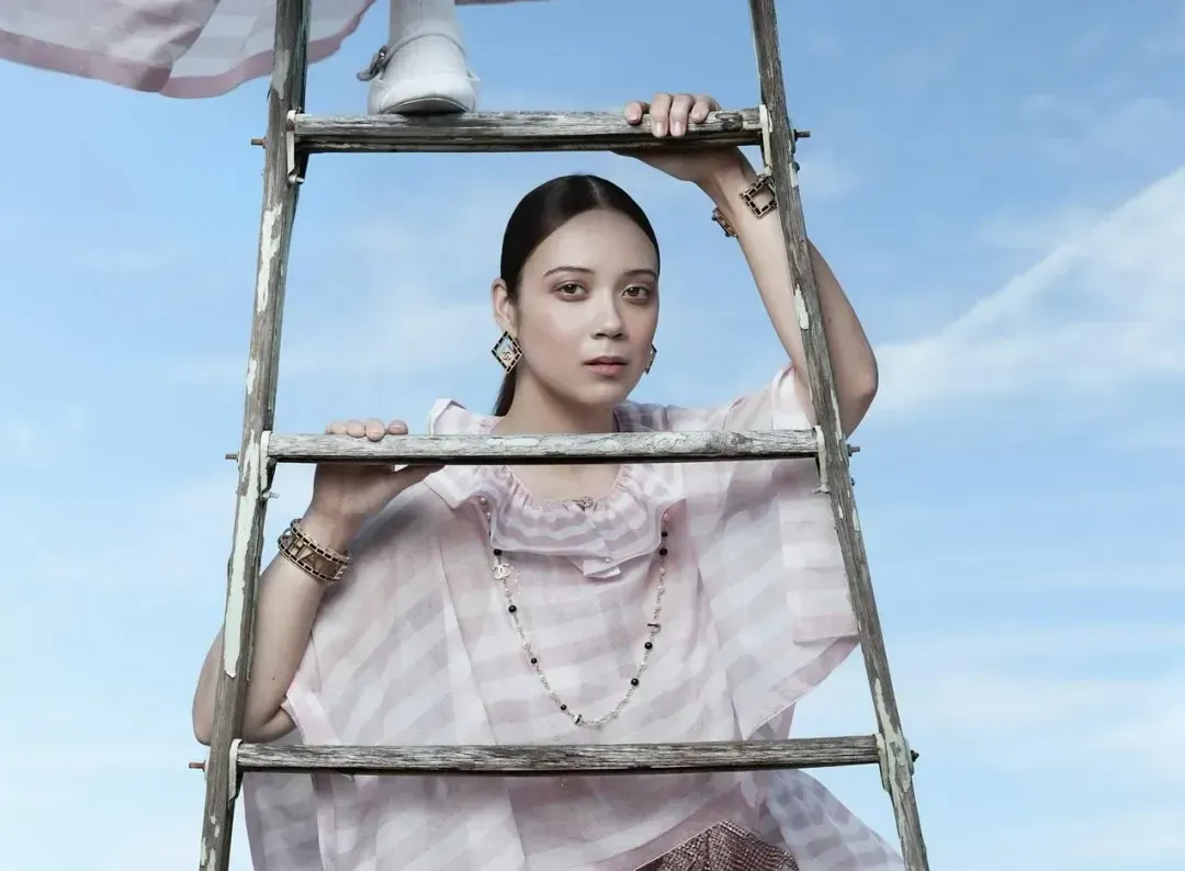 Laufey on the ladder, wearing light pink dress for Vogue China