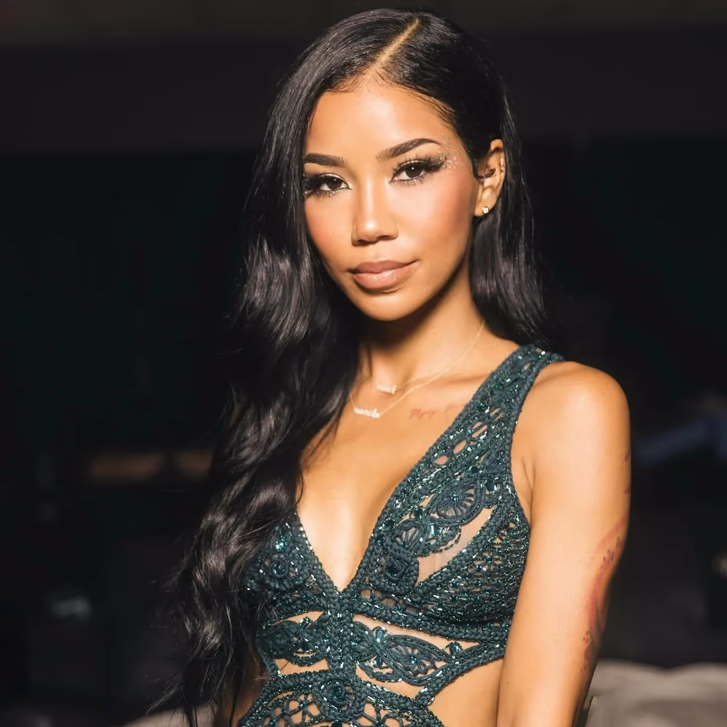 Jhene Aiko in deep decolte green beaded dress, wavy long black hair, artist bio/profile 2024