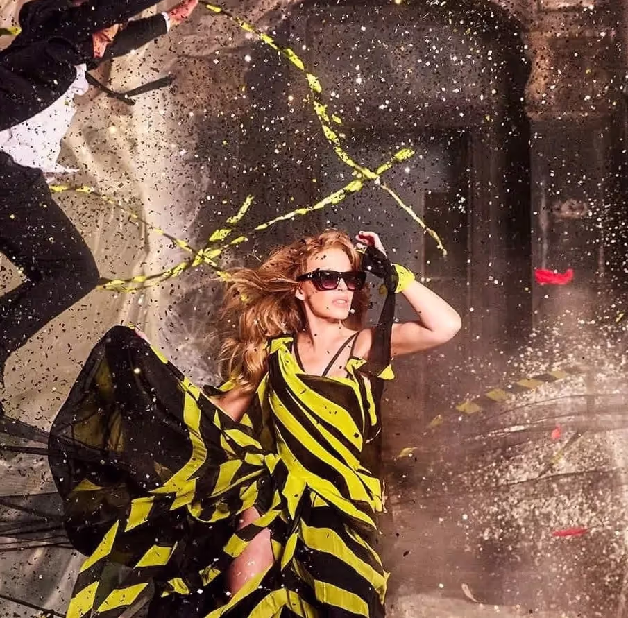 Kylie Minogue mengenakan gaun bergaris kuning dan hitam, mengenakan kacamata di set video musik "Lights, Camera, Action"