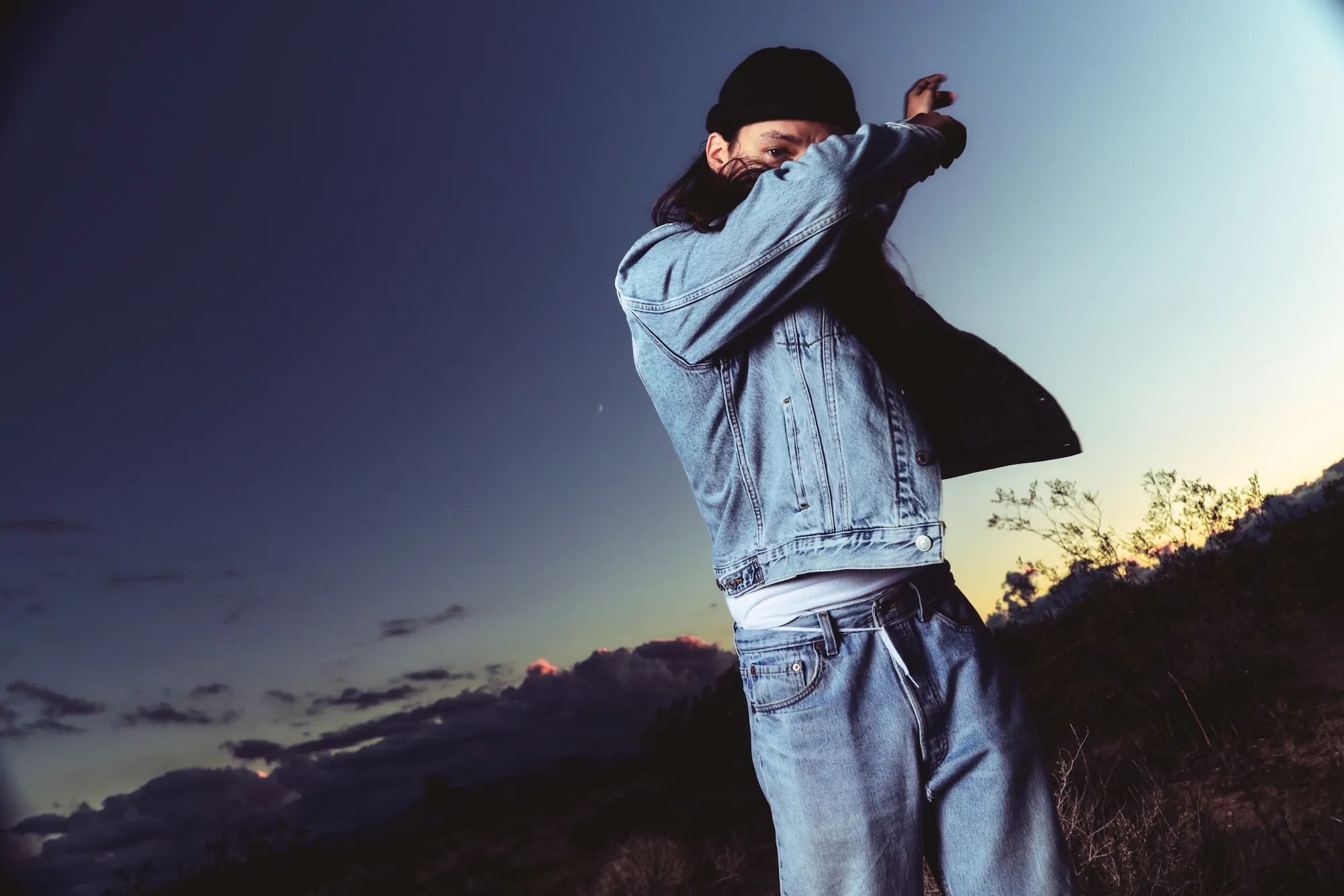 Sunsetto, wearing black hat, jeans, jeans jacket. Photo Credit: @blacksocks.studio