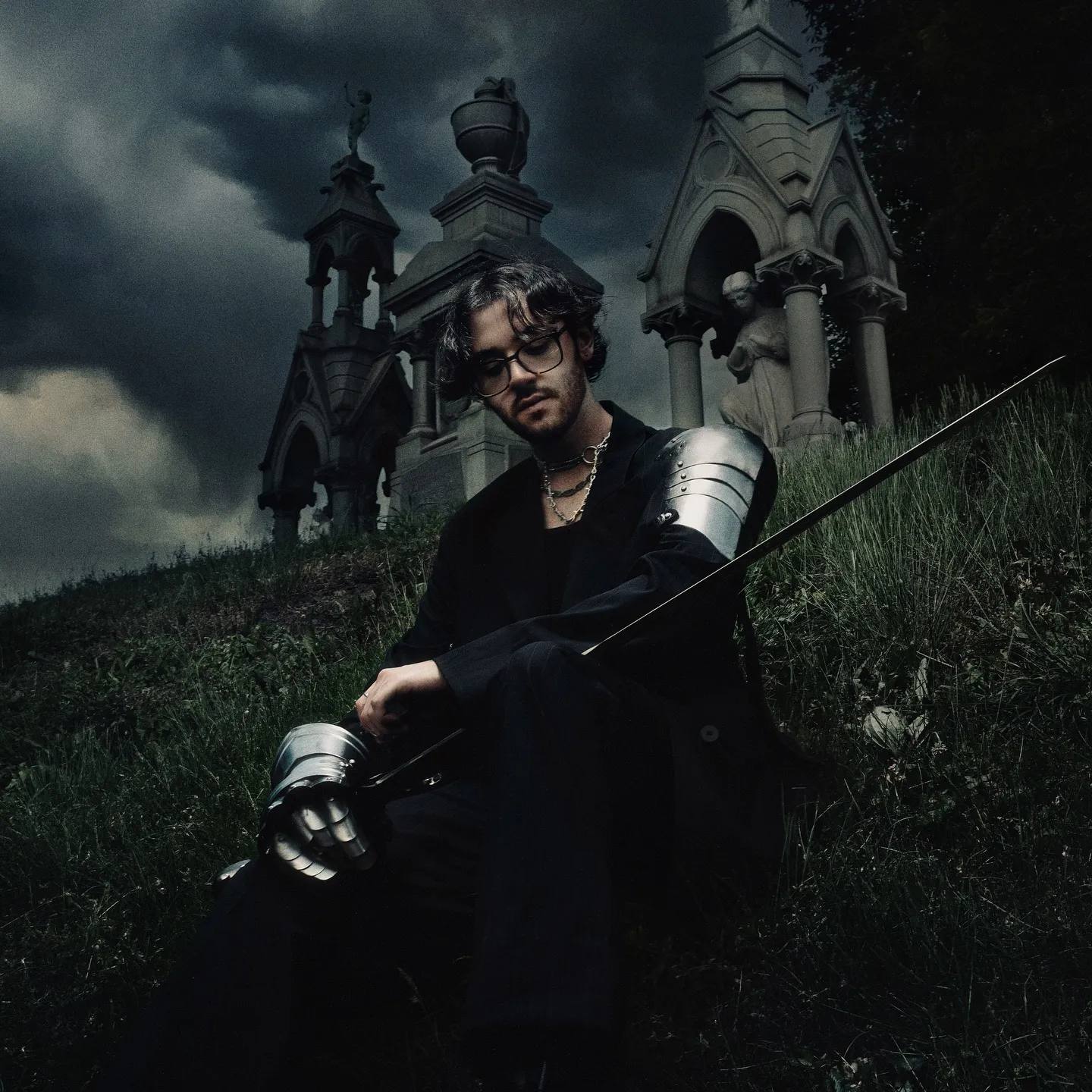 Chris Grey wearing black and silver armor in a foggy cemetery for the press kit of 'The Castle Never Falls'.
