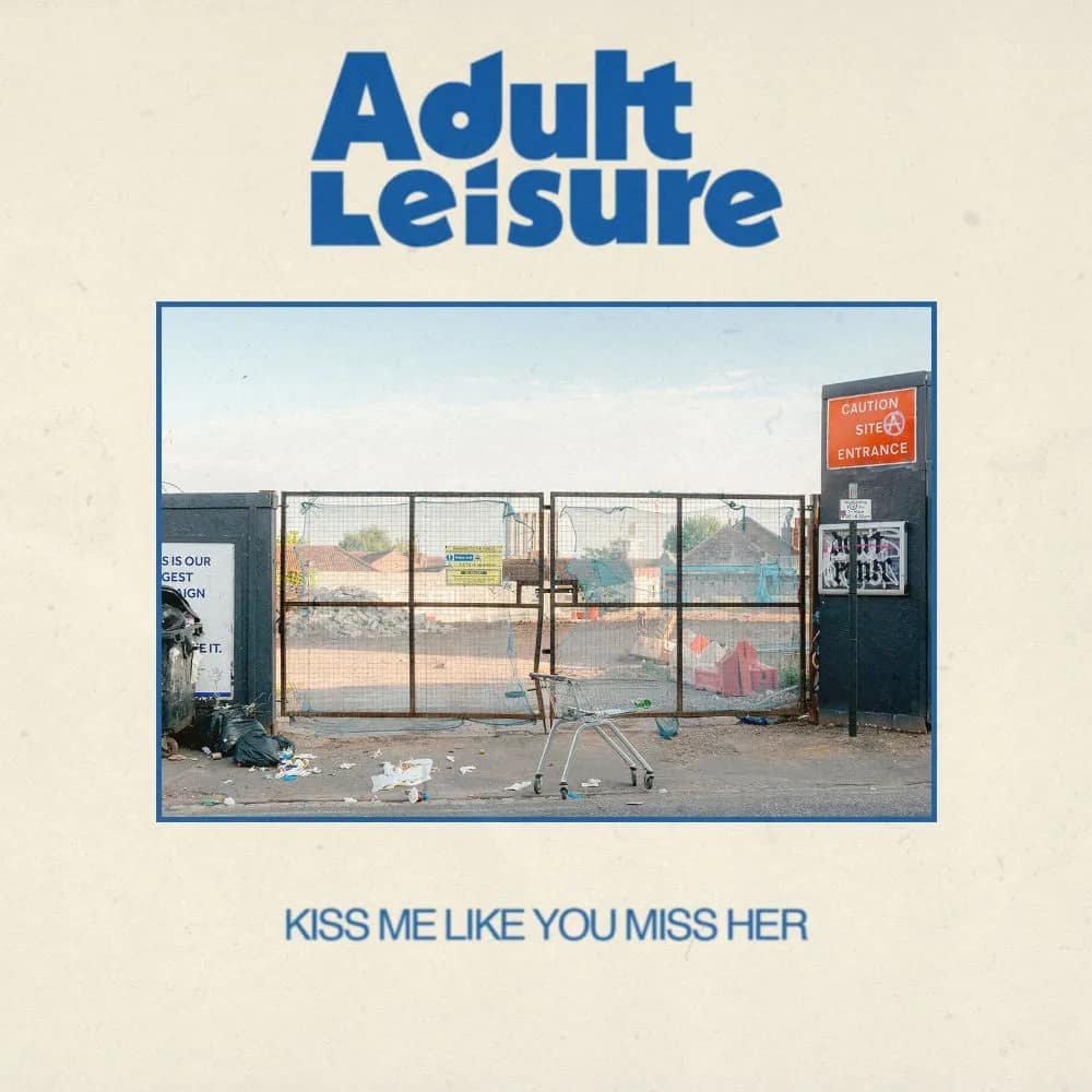 Adult Leisure, "kiss me like you miss me", single cover art: shopping cart on the abundant lot next to the large gate surrounded by garbage.