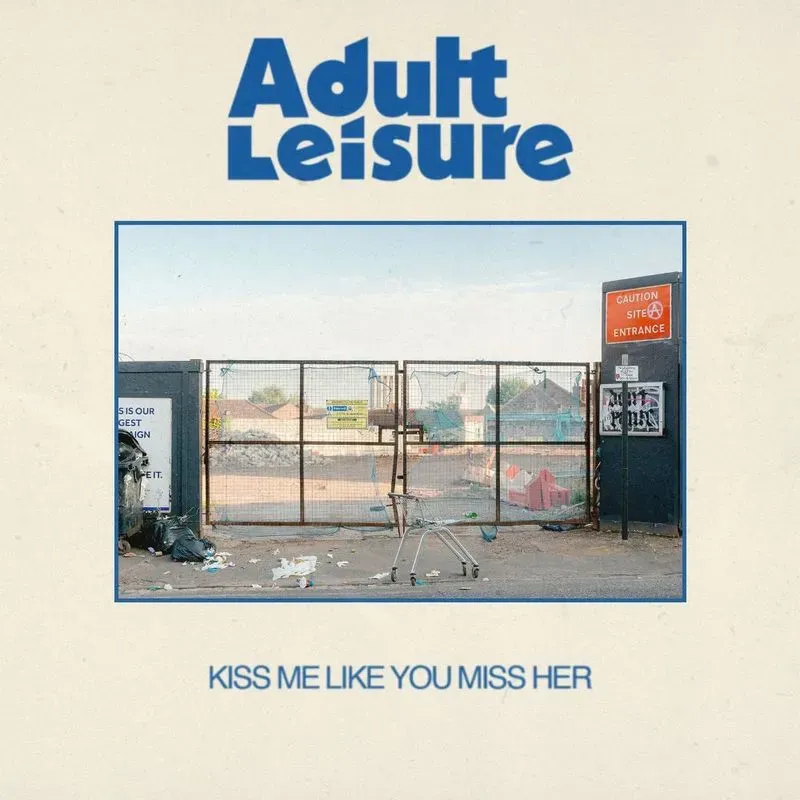 Adult Leisure, "kiss me like you miss me", single cover art: shopping cart on the abundant lot next to the large gate surrounded by garbage.