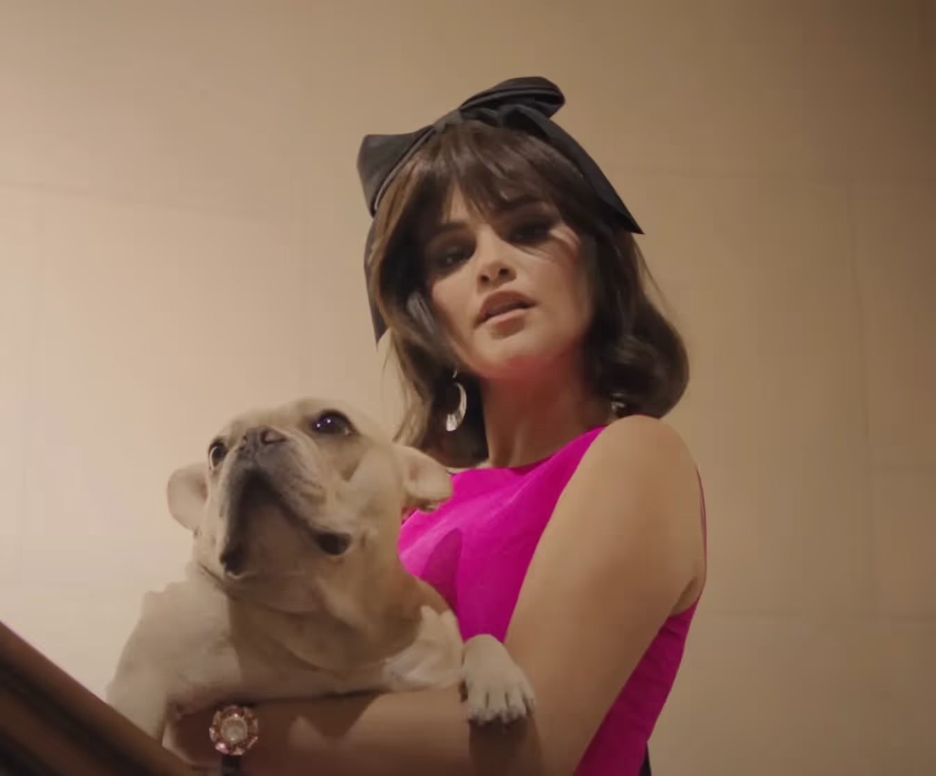 Selena Gomez wearing bright pink dress and a bow, holding a puppy in a "Love On" music video