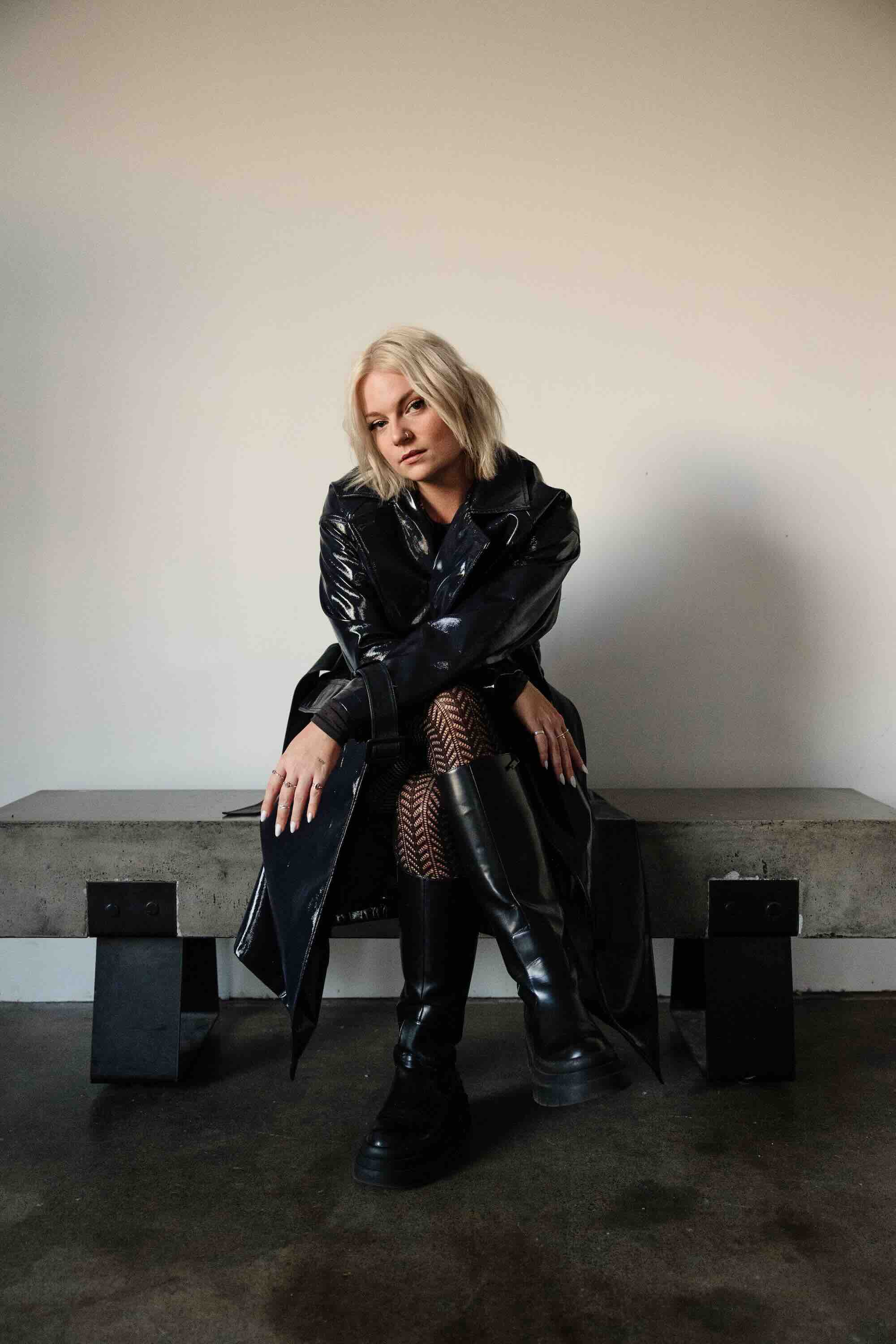 Jessia, in a black leather coat and boots, sitting on a cement bench. Photo credit: Chase Hanssen.